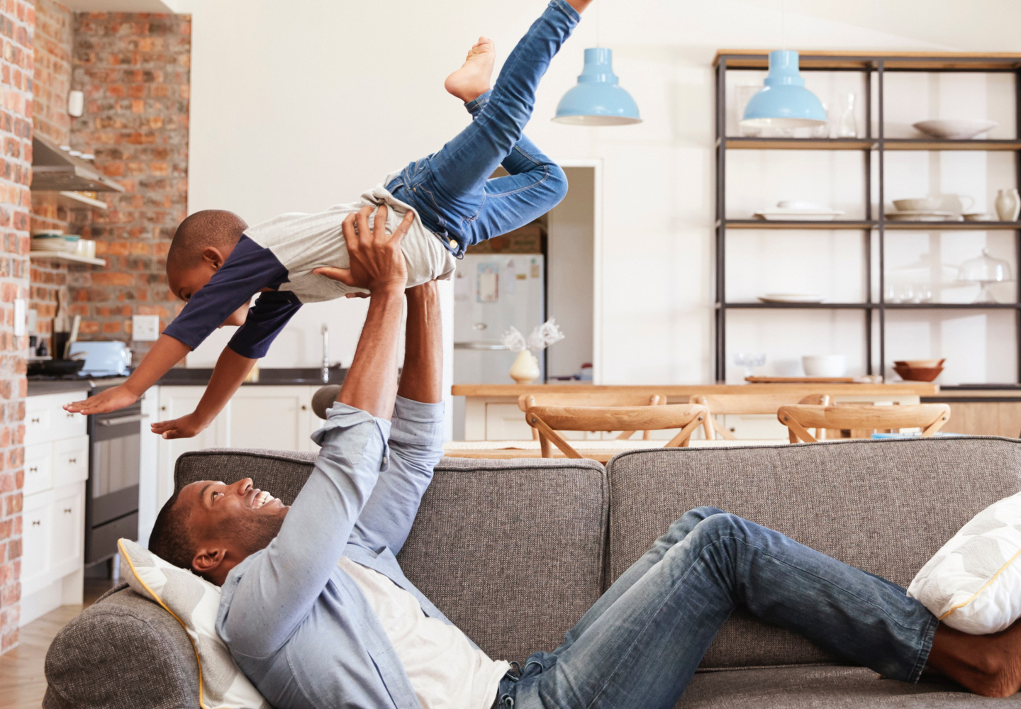 A father laying on the couch holding his son up in the air above him