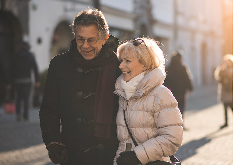 An elderly couple smiling while walking outside in cold weather